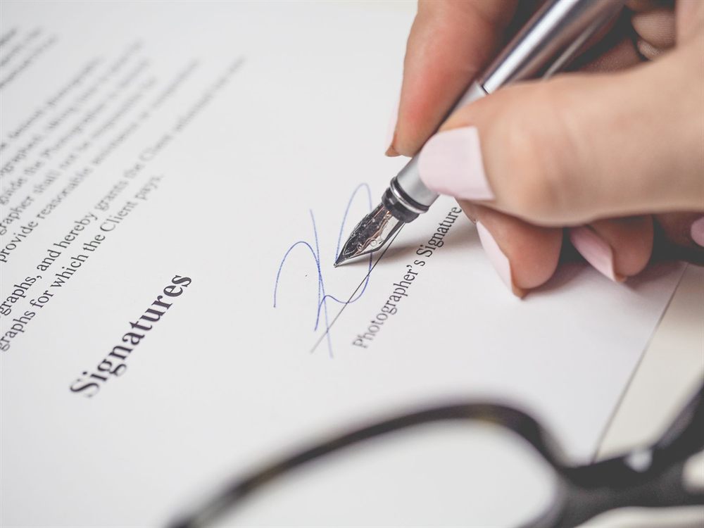 Hand signing a document with a fountain pen beside a pair of glasses