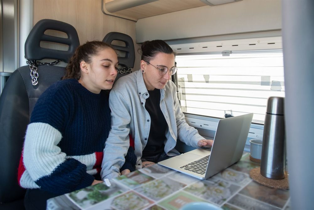 Two women planning a trip together on a laptop with a map on the table