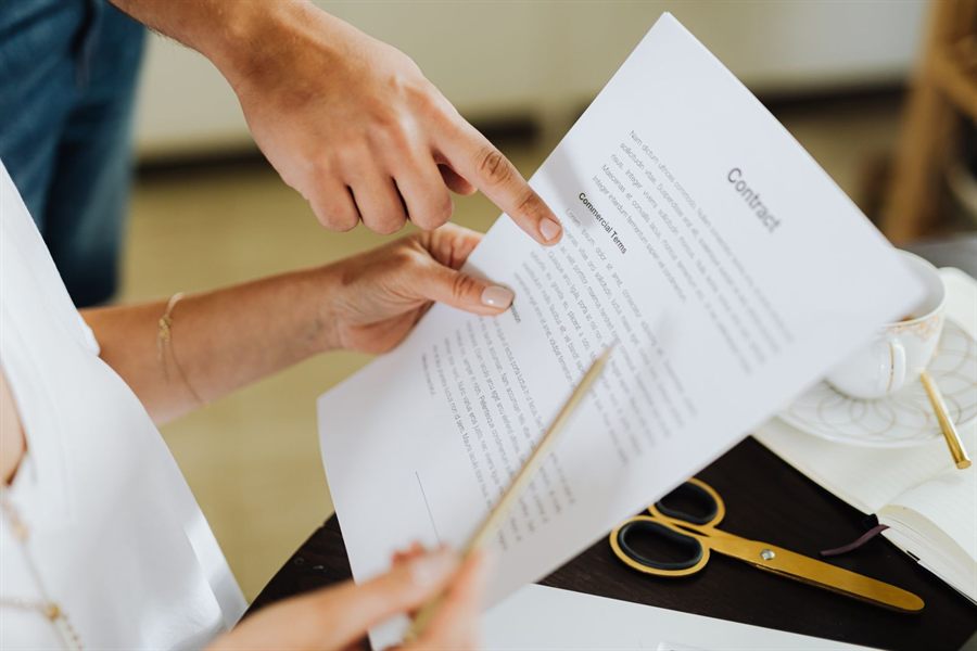 Two people pointing at clauses in a printed contract at a desk