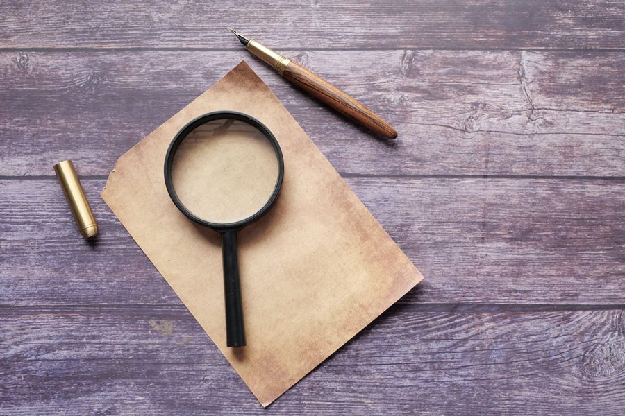 Magnifying glass and quill pen on a sheet of paper on a wooden table