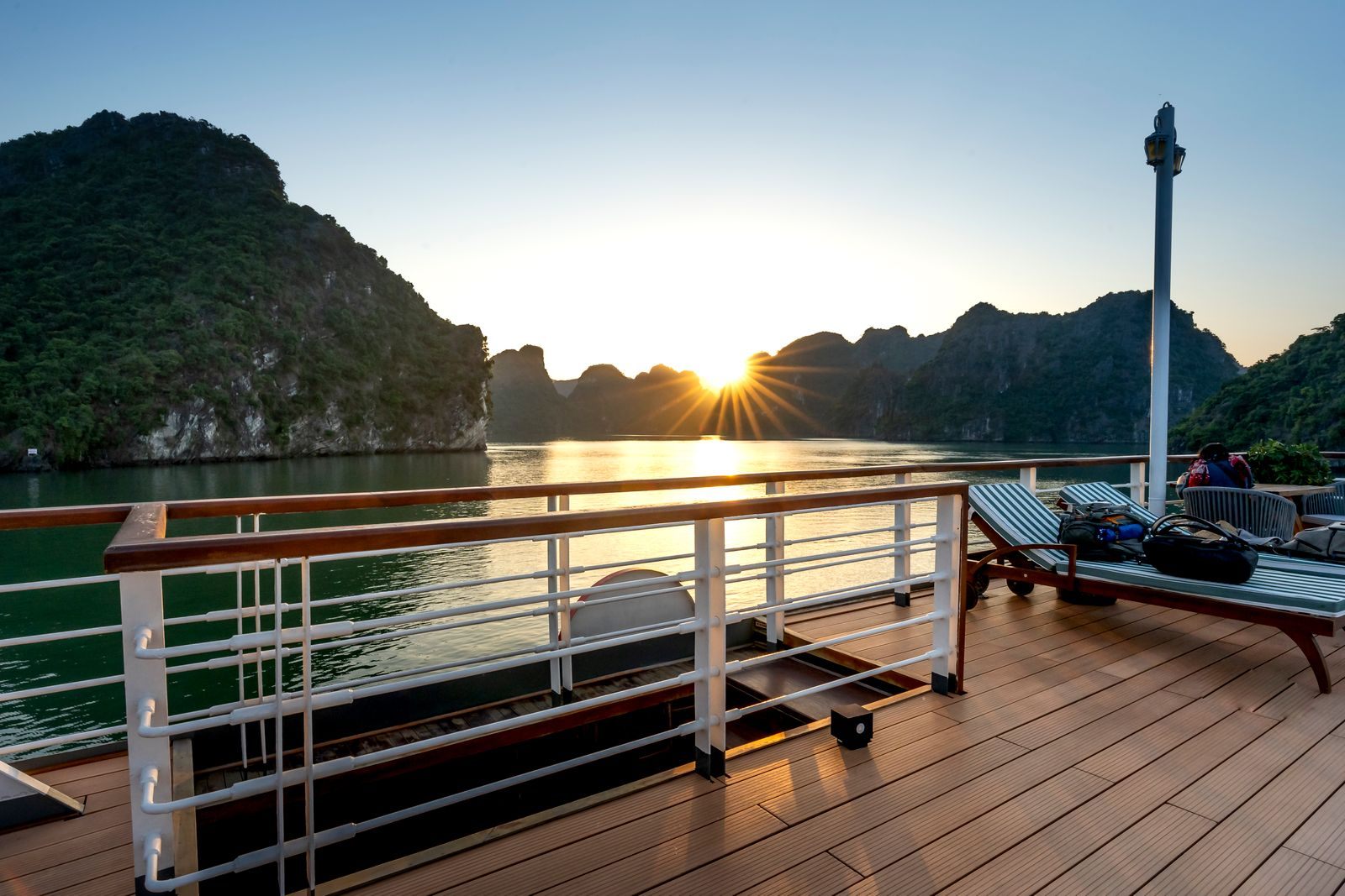 Sunset over a mountain-ringed bay from a ship&rsquo;s teak deck, the kind of view a Celebrity Cruises best price guarantee upgrade might improve
