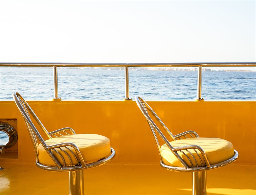 Two yellow deck chairs facing the sea from a ship&rsquo;s railing