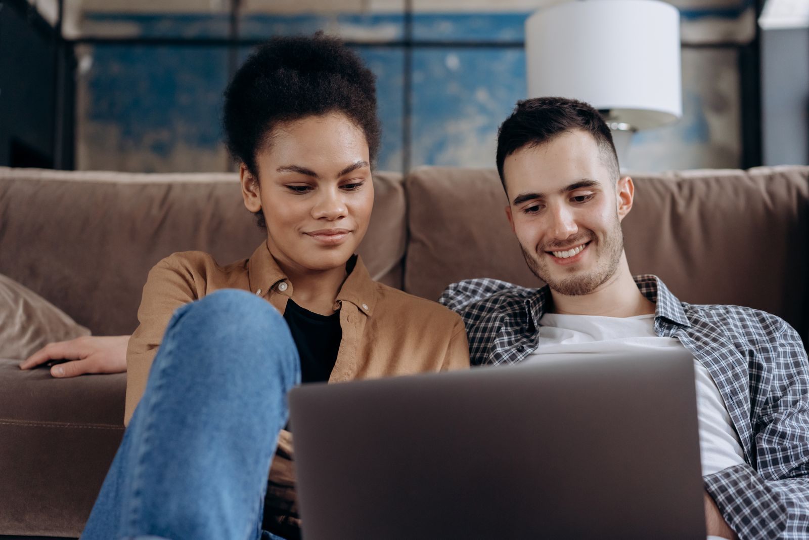 Smiling couple on a sofa comparing cruise price match offers on a laptop